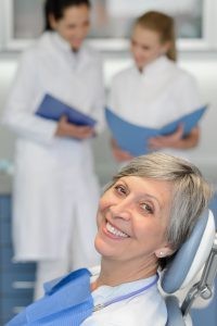Happy Older Female Patient Looking at Camera with Out of Focus Dentists in the Background