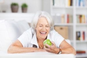 Mature Woman Sitting On White Couch Smiling Holding a Green Apple