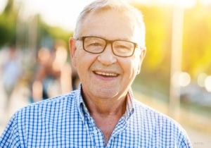 Older Caucasian Male With Glasses and Plaid Shirt Smiling Outdoors 