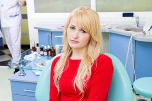 Sad Blond Woman In Red Blouse Sitting In Dental Chair